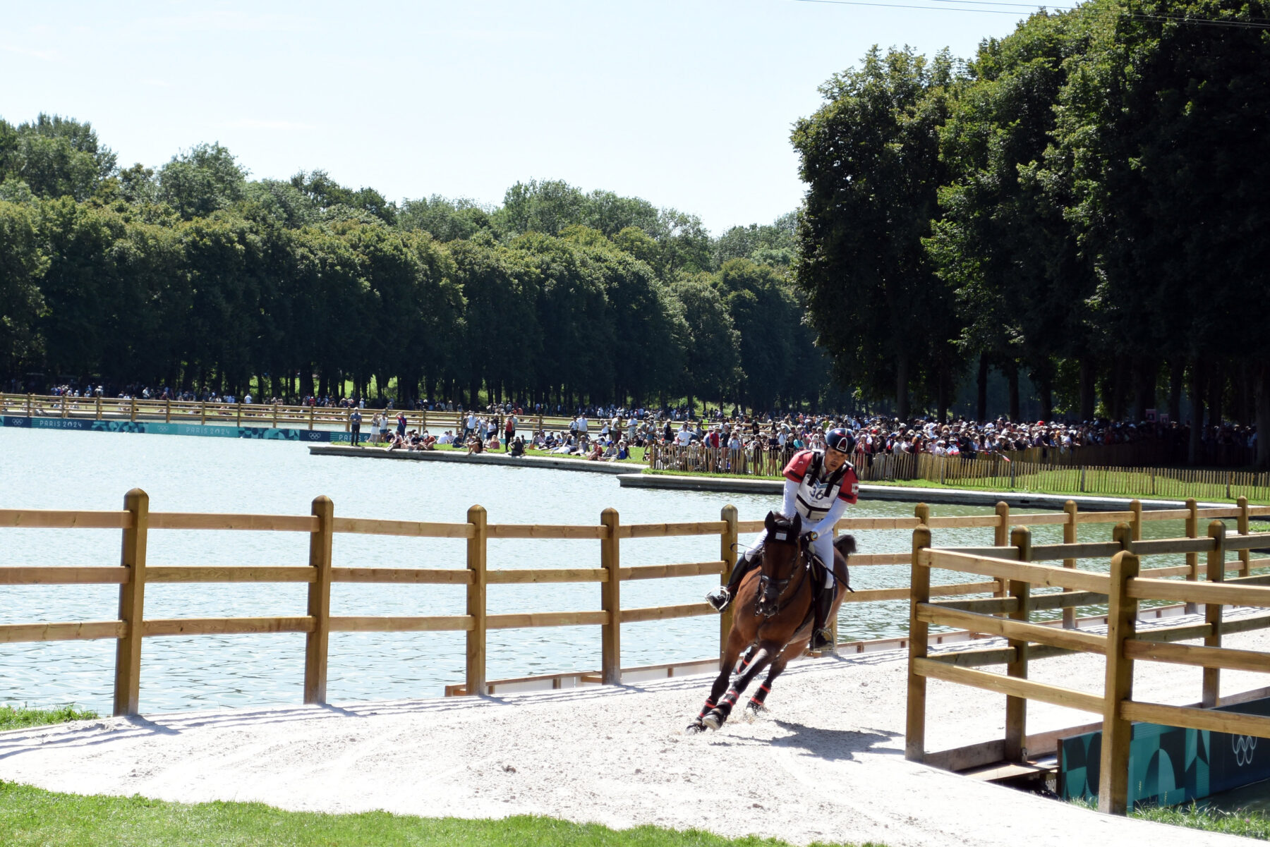 Photo of cross country horseback rider at the grounds of Versailles with water, trees, and spectators in the background