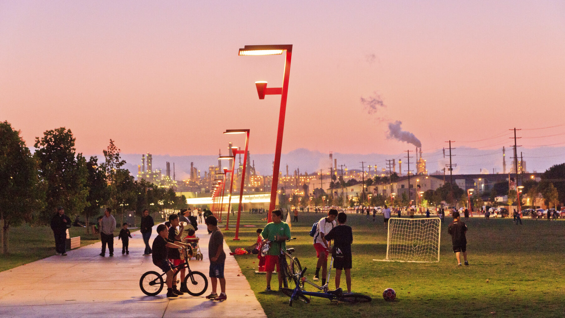 Sunset shot looking back at the park with people on walkway and lawn and streetlights turning on