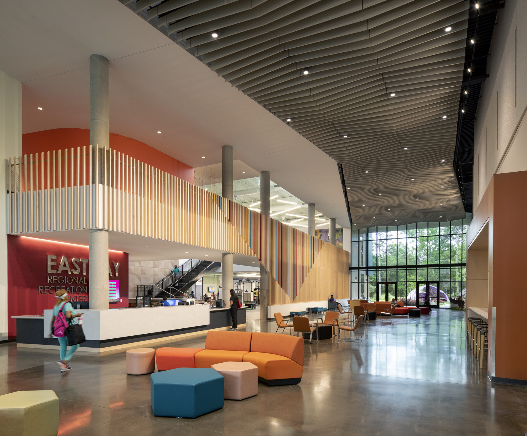 View of Eastway Rec Center lobby with front desk, wood paneled wall and ceiling, movable furniture, and view out to the front main entry exterior.