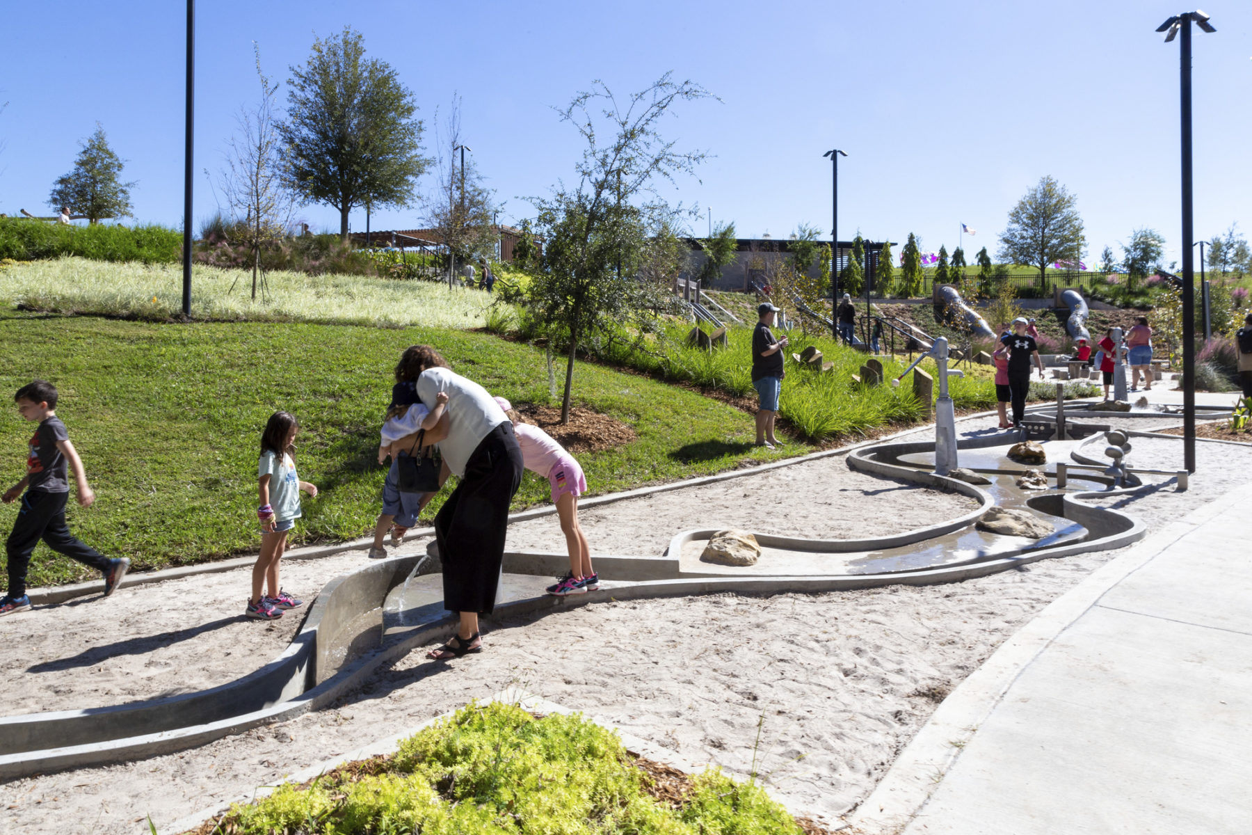 A woman playing with two children in a playspace on a sunny day